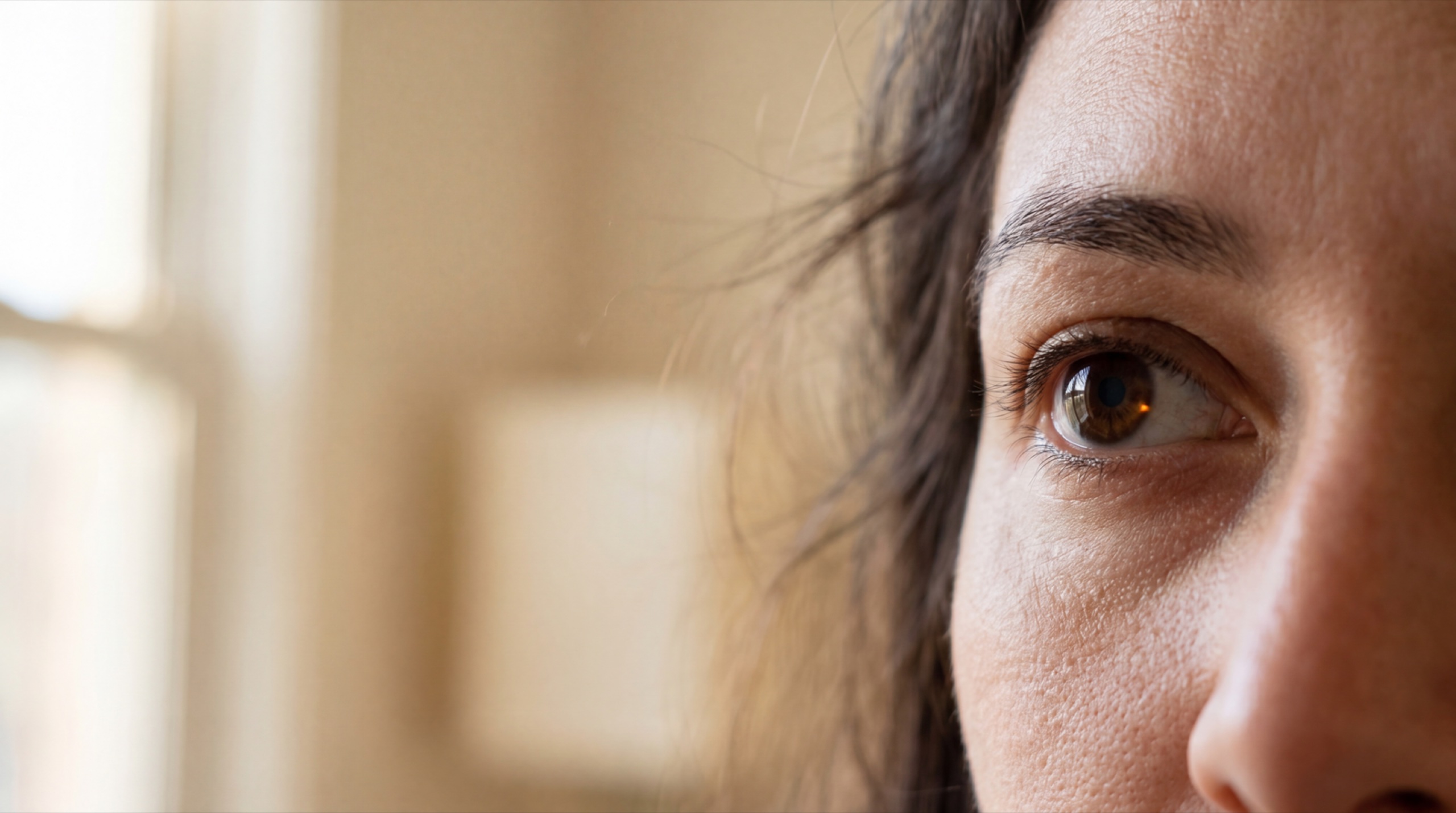 Lena's eye in soft morning light — a barely-visible amber pinpoint inside the iris suggests the smart contact lens has rendered a proposal